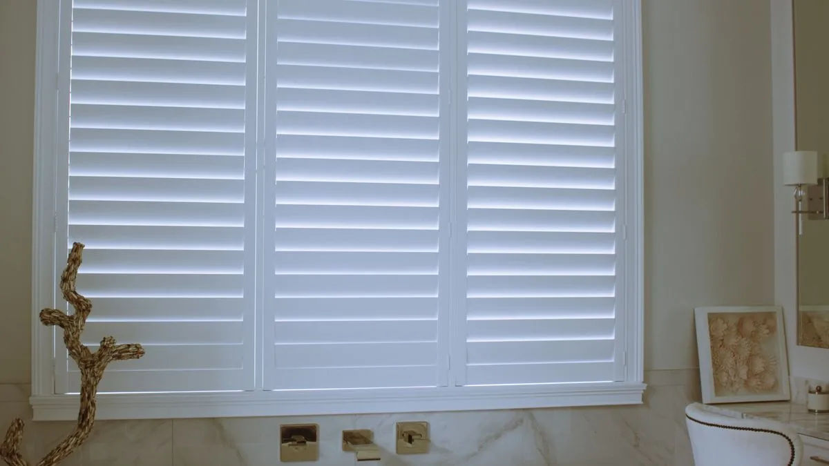 White PVC plantation shutters fitted in a NSW ensuite bathroom showing sealed louvre construction and aluminium reveal suited to wet-room specification